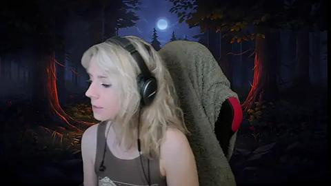 Media: Video of a young blonde woman with headphones, wearing a gray tank top, standing in a dark, forested area with a full moon and glowing red tree roots.