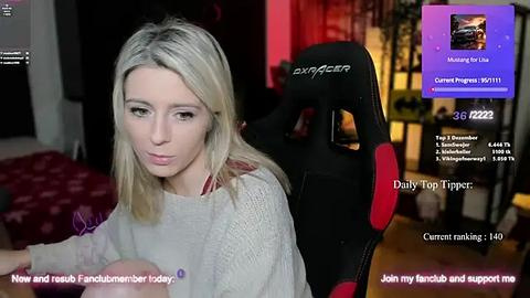 Media: A video of a blonde woman in a grey sweater, seated in a black and red gaming chair, with a live stream overlay.