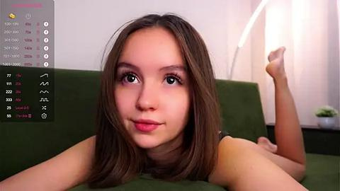 Media: A video of a young, light-skinned, brunette woman lying on her stomach on a green couch, wearing a black top, with a smartphone displaying a calendar app in the background.