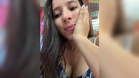 Media: A video of a young woman with long dark hair, wearing a blue lace bra, touching her face, blurred background.
