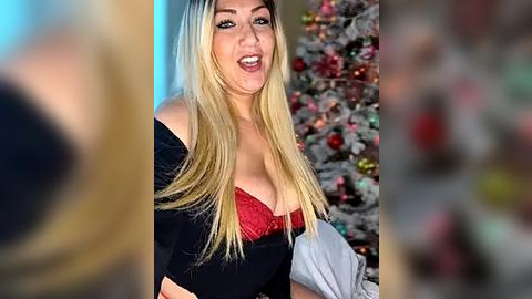 Media: Video of a blonde woman with long hair, wearing a black off-shoulder top and a red lace bra, smiling next to a decorated Christmas tree.