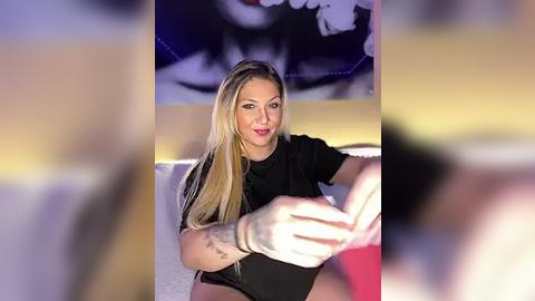 Media: Video of a blonde woman with long hair, wearing a black top, gesturing with her hands, in front of a blurred, colorful abstract background.