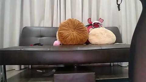 Media: Video of a plush brown cushion on a modern, dark brown leather sofa, adorned with a fluffy white owl and a red bow, against white curtains in a minimalist living room.