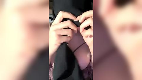 Media: A video featuring a close-up of a person's hands in black clothing, focusing on buttoning a shirt. The background is blurred, emphasizing the hands and clothing.