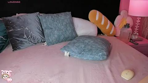 Media: Video of a cozy, pink-themed bedroom with a bed adorned with blue and white pillows, a stuffed animal, and a lamp.