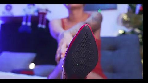 Media: Video of a close-up of a woman's red high-heeled shoe with a detailed sole, set against a blurred festive background with Christmas decorations and a tree.