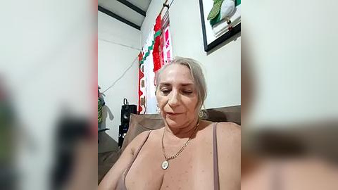 Media: Video of a middle-aged, light-skinned woman with shoulder-length gray hair, wearing a revealing, low-cut top, sitting indoors with a neutral expression.