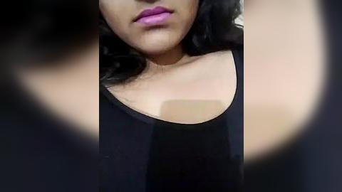 Media: Close-up video of a young woman with medium brown skin, wearing a black tank top, showing off her dark, wavy hair and bright pink lipstick.