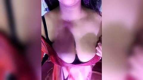 Media: Video of a topless woman with large breasts, partially wearing a red lace bra, taken from a low angle, with blurred faces in the foreground.