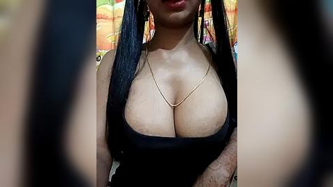 Media: Video of a light-skinned woman with long black hair, wearing a black tank top that accentuates her large breasts, against a colorful, patterned backdrop.