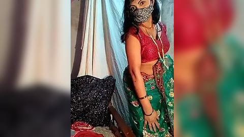 Media: Video of an Indian woman wearing a red sequined blouse, green saree, and leopard print face mask, standing in a room with colorful curtains and a black bag.