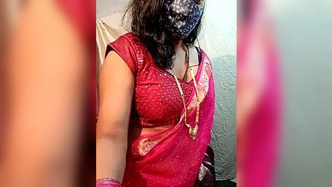 Media: A video of a woman with medium skin tone wearing a red saree with gold embroidery, a face mask, and a silver necklace, blurred background.