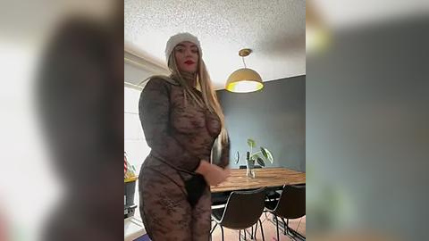 Media: Video of a blonde woman in a sheer, lace bodysuit with a white knit hat, standing in a modern dining room with wooden table, chairs, and potted plants.