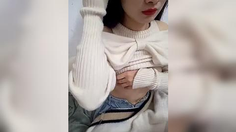 Media: A video of an East Asian woman with fair skin, wearing a white knitted sweater pulled up to expose her small breasts, denim shorts, and red lipstick. Background is blurred.