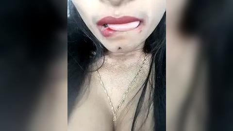 Media: A close-up video of a woman with light skin and long black hair, wearing a gold necklace, sticking out her tongue and showing her cleavage.