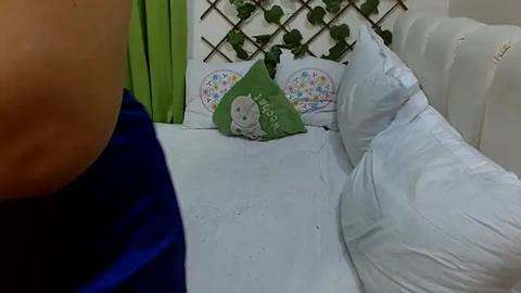 Media: Video of a child's bed with a green pillow featuring a cute cartoon bunny, surrounded by white pillows and a white headboard with green curtains and ivy vines.