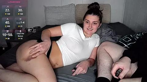 Media: A video of a smiling, white woman with a medium build, wearing a white crop top and black panties, lying on a bed with a man, partially dressed, beside her.