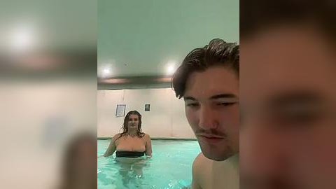 Media: Video of a young woman with wet hair and a man in a pool, both partially submerged, with a blurred person in the background.