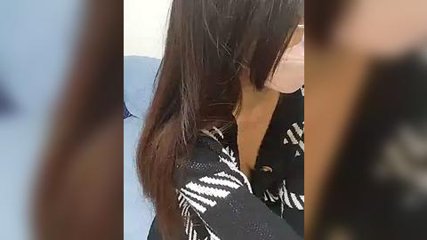 Media: Video of a woman with long brown hair wearing a black and white patterned blouse, seen from the side, partially blurred.