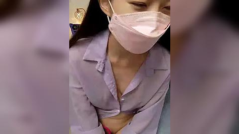 Media: A video of an Asian woman in a lavender button-down shirt with a pink face mask, partially unbuttoned, revealing cleavage. The background is blurred, showing a kitchen with a heart-shaped decoration.