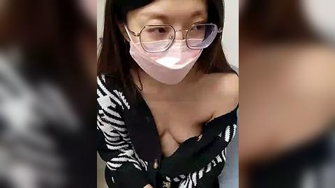 Media: A video of an East Asian woman with straight brown hair, wearing glasses and a pink surgical mask, exposing her cleavage in a black and white patterned top, blurred background.