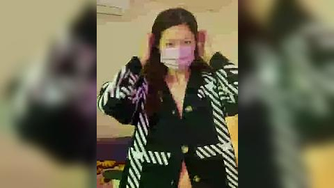 Media: Video of an Asian woman with long black hair, wearing a black and white striped coat, white mask, and pink gloves, standing indoors with blurred background.