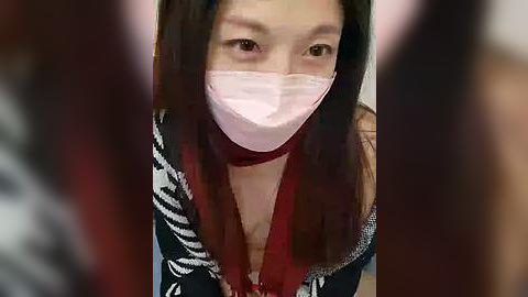 Media: Video of an East Asian woman with long, straight dark hair, wearing a pink surgical mask, black blouse, and red scarf, blurred background.