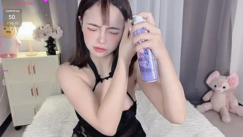 Media: A video of an Asian woman with shoulder-length black hair, wearing a black lace lingerie top, spritzing her hair with a blue hair spray, in a modern bedroom with gray curtains, white dresser, and a stuffed bunny.