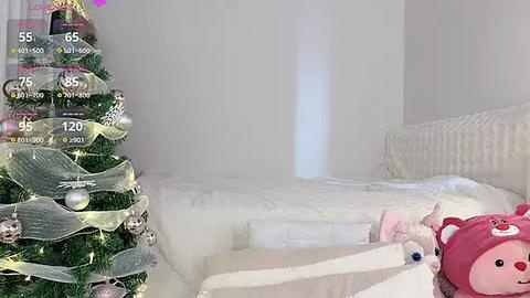 Media: Video of a minimalist, white bedroom with a cozy, snow-covered Christmas tree and a plush pink bear in the foreground.