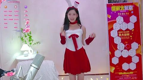 Media: Video of an Asian woman in a red bunny costume, standing in a bright room with a calendar and floral arrangement.