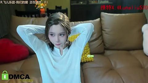 Media: A video of a young girl with long brown hair, wearing a white long-sleeve shirt, lying on a beige leather couch. She has a serene expression. A yellow cushion is beside her.