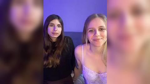 Media: Video of two women with long hair, one in a black top, the other in a lace top, smiling. Background is blurred, with purple lighting.