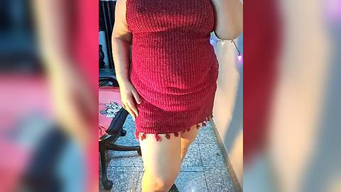 Media: Video of a woman in a red ribbed dress, partially exposing her thighs, standing on a patio with a blurred background.