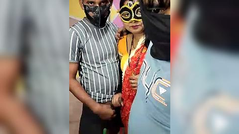 Media: Video of three people in a crowd, one with a black face mask and striped shirt, another in a red and orange sari, and a third in a light blue shirt.