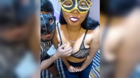 Media: Video of a woman in a black lace bra, gold mask, and blue jeans, standing with a man wearing a zebra print shirt and black mask.