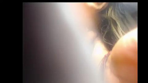 Media: Video of a close-up, blurred image showing a woman's face with wavy, shoulder-length blonde hair, partially obscured by light, creating a soft, ethereal effect.