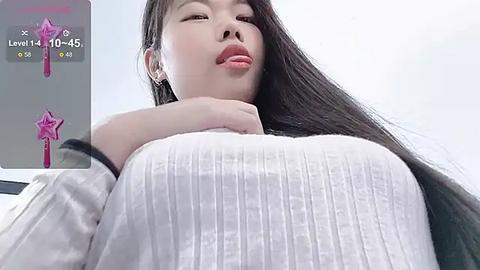 Media: A close-up video of an East Asian woman with long black hair, fair skin, and large breasts, wearing a white ribbed sweater, puckering her lips. Background shows a level 10,45% game screen with pink star icons.