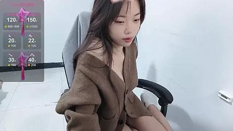 Media: A video of an East Asian woman with long black hair, wearing a brown coat, sitting in a gray chair against a white wall. A weather app with pink accents is displayed on the left.