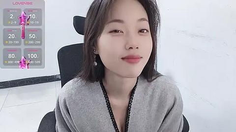 Media: Video of an East Asian woman with straight, shoulder-length black hair, wearing a grey cardigan, sitting on a black chair in a white room. A digital overlay displays \"Low Viscosity\" with a pink liquid and thermometer.