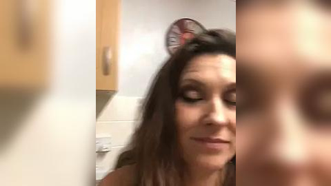 Media: A video of a woman with long dark hair and a cat ear headband, smiling in a bathroom with wooden cabinets and a tiled wall.