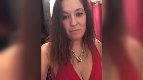 Media: Video of a middle-aged woman with long brown hair, wearing a red halter top, standing in a bathroom with a red shower curtain and blurred background.