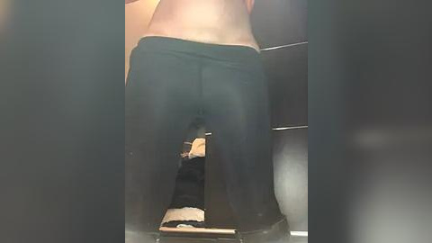 Media: A video shows a person's lower back and buttocks in black leggings, squatting over a toilet seat with a black cat on the floor. The background is a bathroom with beige tiles and a dark countertop.