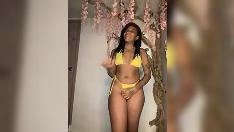 Media: Video of a curvy, dark-skinned woman in a yellow bikini, striking a pose with hands on hips, surrounded by pink cherry blossom decor.