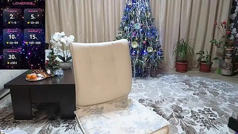 Media: Video of a Christmas-themed living room with a cream-colored armchair, white orchid plant, and a decorated tree, set against a backdrop of beige curtains.