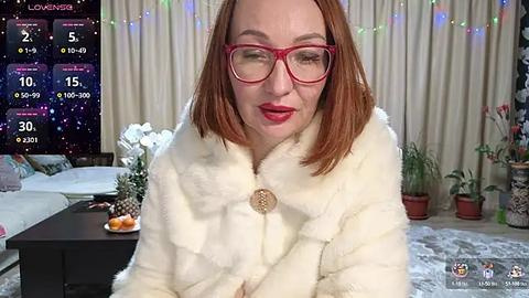 Media: Video of a red-haired woman with fair skin, wearing red glasses and a white fur coat, indoors with a cozy, festive room in the background.