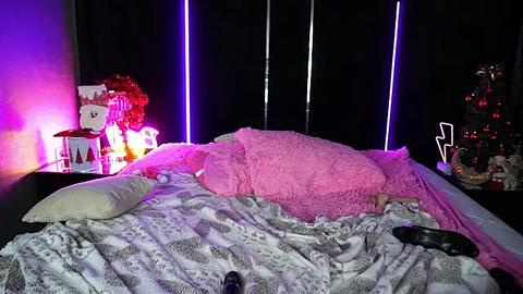 Media: A video of a dimly lit bedroom with a messy bed, featuring pink and white bedding, a plush pillow, and a TV remote on the blanket. Black curtains with vertical purple LED lights create a moody ambiance.