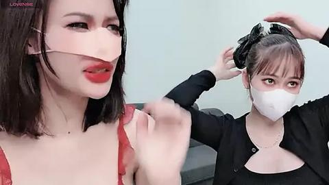 Media: Video of a woman with pale skin, wearing a red lace dress and white mask, having her hair styled by another masked woman in black.