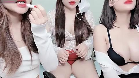 Media: Three Asian women with long hair and pale skin, wearing white tops, black bras, and red panties, engaging in playful, intimate behavior, set against a soft, light background.