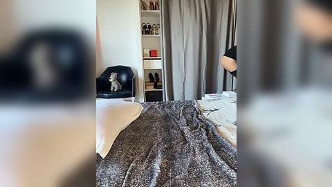 Media: Video of a modern bedroom with a gray bedspread, black chair, white shelves, and a person partially visible in the background.