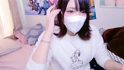 Media: A video of an Asian woman with shoulder-length black hair, wearing a white face mask and a graphic t-shirt, adjusting her hair, in a cozy, cluttered bedroom with posters and a bed.